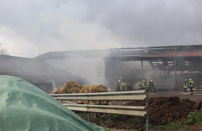 Szene nach dem Großbrand mit Feuerwehrleuten, die vor und in der Stallung im Rauch stehen.