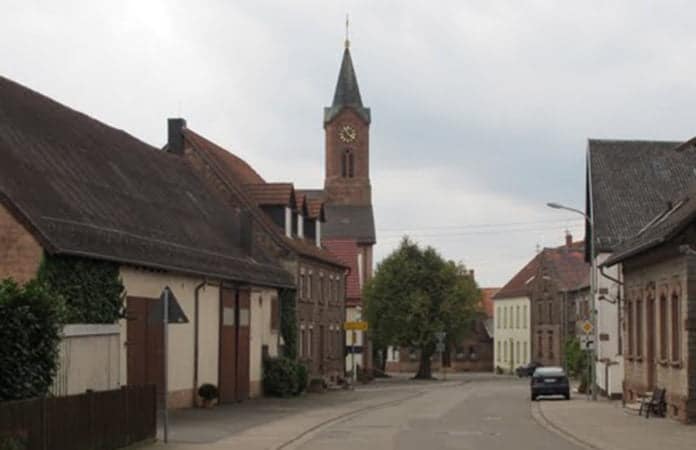 Eine Straße zur Reichenberger Kirche, die von einer Fliegenplage heimgesucht wurde. Rechts und links von ihr stehen Häuser und der Himmel ist bedeckt.
