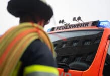 Nach Brand von Wohnhaus: Feuerwehr findet totes Ehepaar Ein Feuerwehrmann mit Schlauch vor einem Feuerwehr-Auto