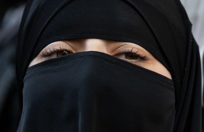 Nahaufnahme einer Frau mit schwarzem Niqab, der nur ihre Augenpartie sichtbar lässt. Das Bild symbolisiert Themen wie Religionsfreiheit, Verhüllung und gesellschaftliche Debatten.