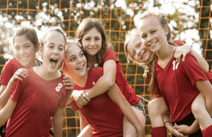 Lachende Mädchen-Fußballmannschaft in roten Trikots vor Tor mit Netz, Symbolbild für Teamgeist und Sportförderung durch Trikotaktion der Sparkasse Trier.
