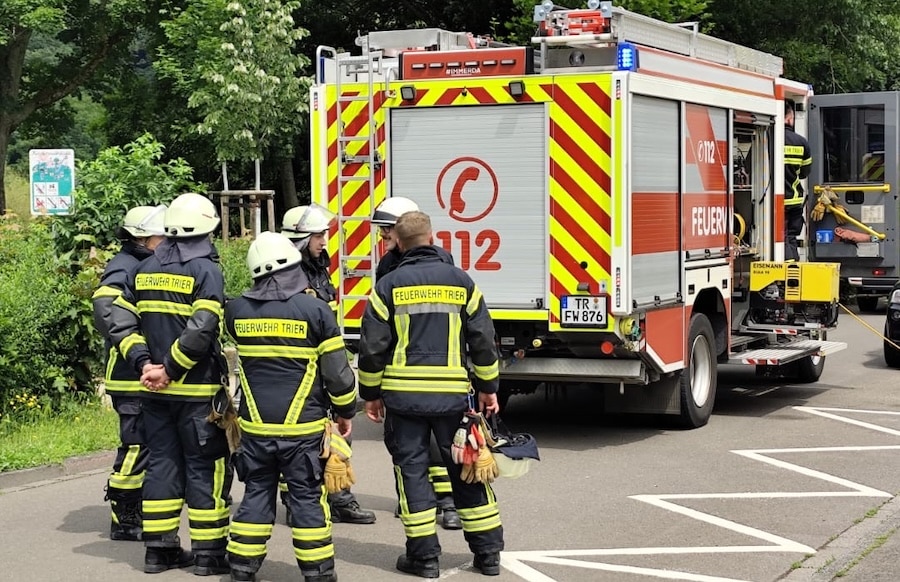 Rückansicht eines Feuerwehreinsatzes: Feuerwehrleute stehen hinter einem Einsatzfahrzeug mit offener Ausrüstung, Einsatz in Trier.