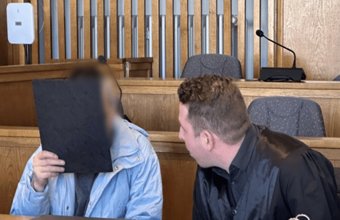 Angeklagter sitzt mit seinem Verteidiger im Gerichtssaal; das Gesicht des Angeklagten ist durch eine Mappe verdeckt – Beginn eines Strafprozesses.