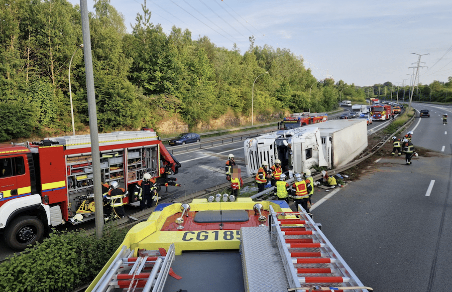 Ein umgekippter Sattelanhänger auf einer Autobahn bei Nacht. Wassermelonen liegen verstreut auf der Fahrbahn. Rettungs- und Bergungsfahrzeuge mit Blaulicht sind im Hintergrund zu sehen. Quelle: CDGIS
