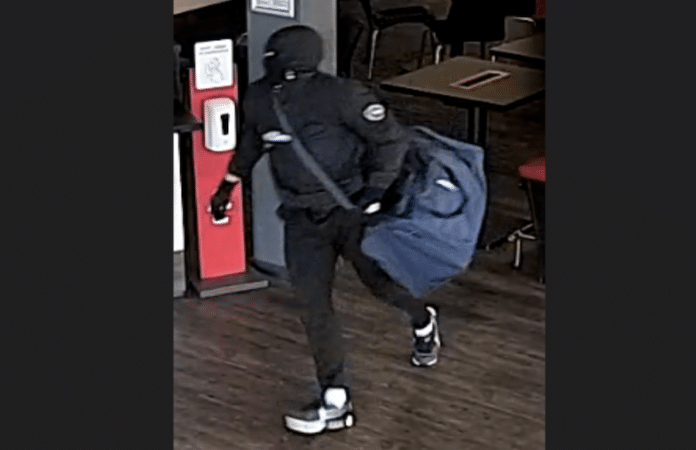 Überwachungskamera zeigt maskierten Täter in schwarzer Kleidung und mit blauer Sporttasche während eines Raubüberfalls in Trier. (Foto: Polizei)