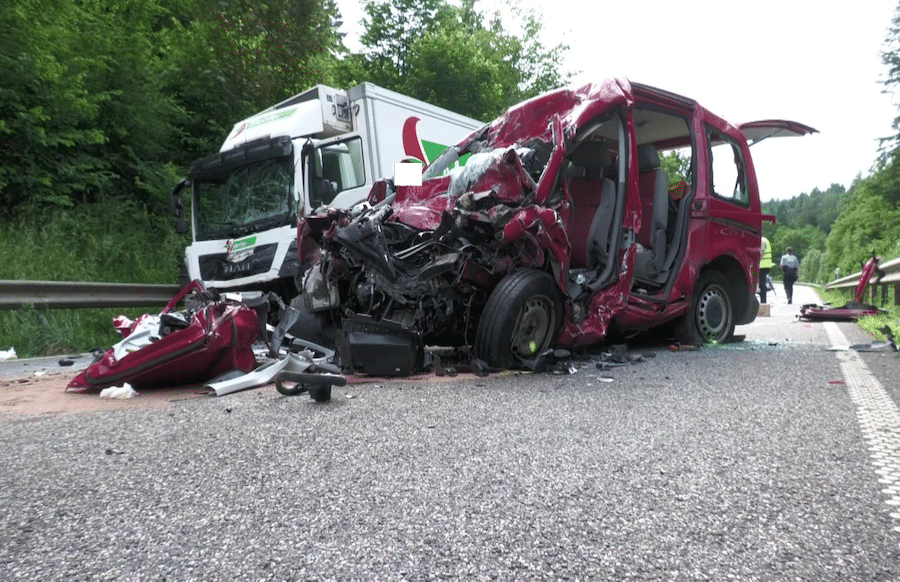 Nahaufnahme eines schweren Verkehrsunfalls mit zerdrücktem roten Van und beschädigtem weißen LKW, Unfall auf Asphaltstraße im Grünen.