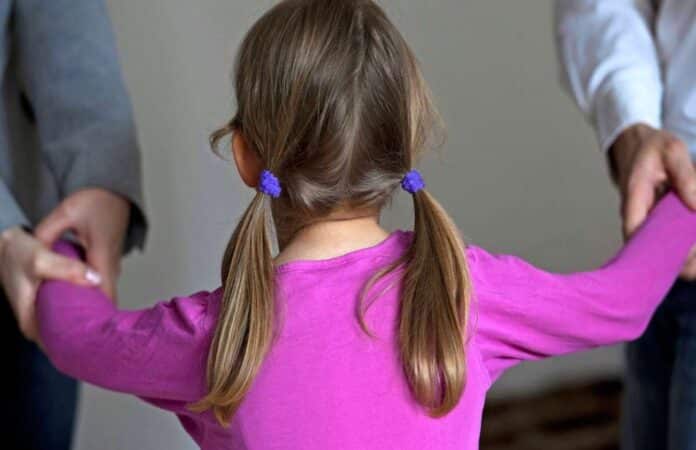 „Symbolbild: Mädchen in lila Shirt wird von beiden Elternteilen an den Armen festgehalten – Darstellung eines Sorgerechtskonflikts bei Scheidung“
