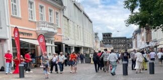 ++ Aktuell: Polizei überwältigt Mann mit Messer in der Trierer Simeonstraße – Schüsse gehört ++ Menschen flanieren an einem Sommertag durch die Simeonstraße in Trier mit Blick auf die Porta Nigra im Hintergrund; moderate Fußgängerfrequenz bei leicht bewölktem Himmel.