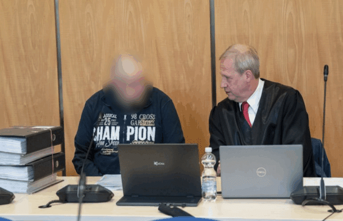 Der Angeklagte sitzt auf einer Gerichtsbank mit seinem Verteidiger