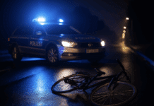 Trier: Radfahrer knall mit über 2,2 Promille in geparktes Auto – Krankenhaus! Ein Polizeiwagen mit Blaulicht steht nachts auf nasser Straße, davor liegt ein umgestürztes Fahrrad – Symbolbild für Fahrradunfall in Trier.