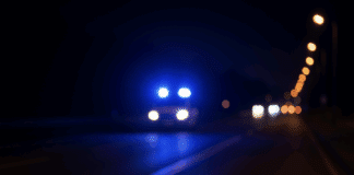 Karnevals-Rückweg endet in Tragödie: 17-Jähriger von Auto erfasst – Lebensgefahr! Dunkle Landstraße bei Nacht mit blauem Blaulicht eines Polizeiwagens – Symbolbild für eine Verfolgungsjagd auf der B41 bei Bad Kreuznach.