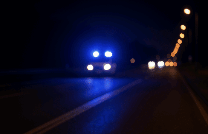 Dunkle Landstraße bei Nacht mit blauem Blaulicht eines Polizeiwagens – Symbolbild für eine Verfolgungsjagd auf der B41 bei Bad Kreuznach.