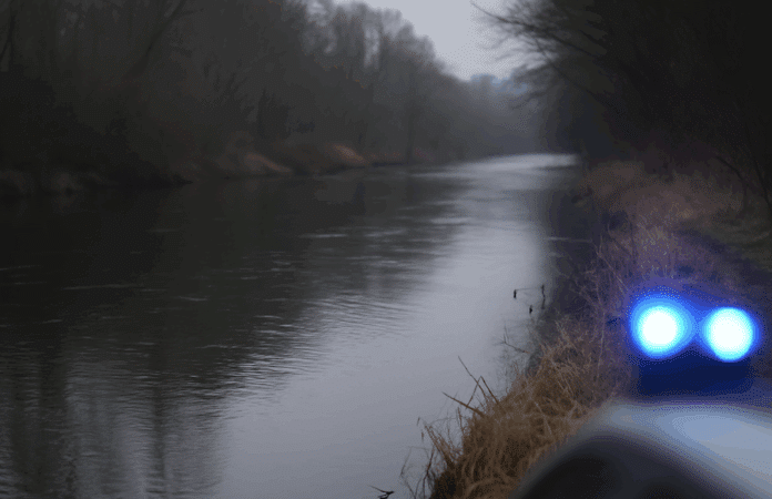 Symbolbild: Flussufer der Prüm an einem trüben Herbsttag, Polizeiabsperrung und Blaulichtreflexionen deuten auf einen Einsatz hin.