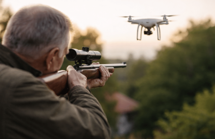 Älterer Mann zielt mit Gewehr auf fliegende Drohne über einem Grundstück als Symbolbild für Drohnen-Vorfall in Frankreich