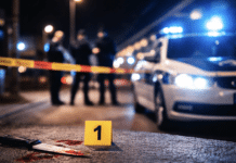 RLP: Mehrmals in Oberkörper gestochen – 23-Jähriger bei Messerattacke am Bahnhof schwer verletzt! Polizeiauto mit Blaulicht und abgesperrter Tatortbereich bei Nacht, unscharfe Einsatzkräfte im Hintergrund als Symbolbild für eine Messerattacke