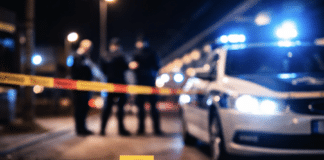 RLP: Mehrmals in Oberkörper gestochen – 23-Jähriger bei Messerattacke am Bahnhof schwer verletzt! Polizeiauto mit Blaulicht und abgesperrter Tatortbereich bei Nacht, unscharfe Einsatzkräfte im Hintergrund als Symbolbild für eine Messerattacke